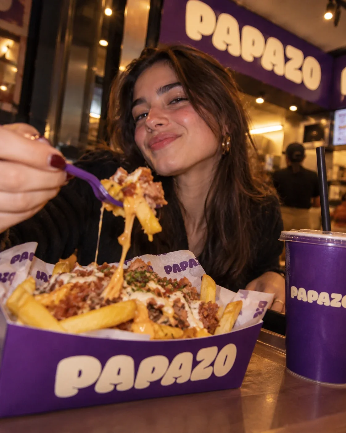 Clienta sonriendo a cámara con un tenedor de salchipapa PAPAZO